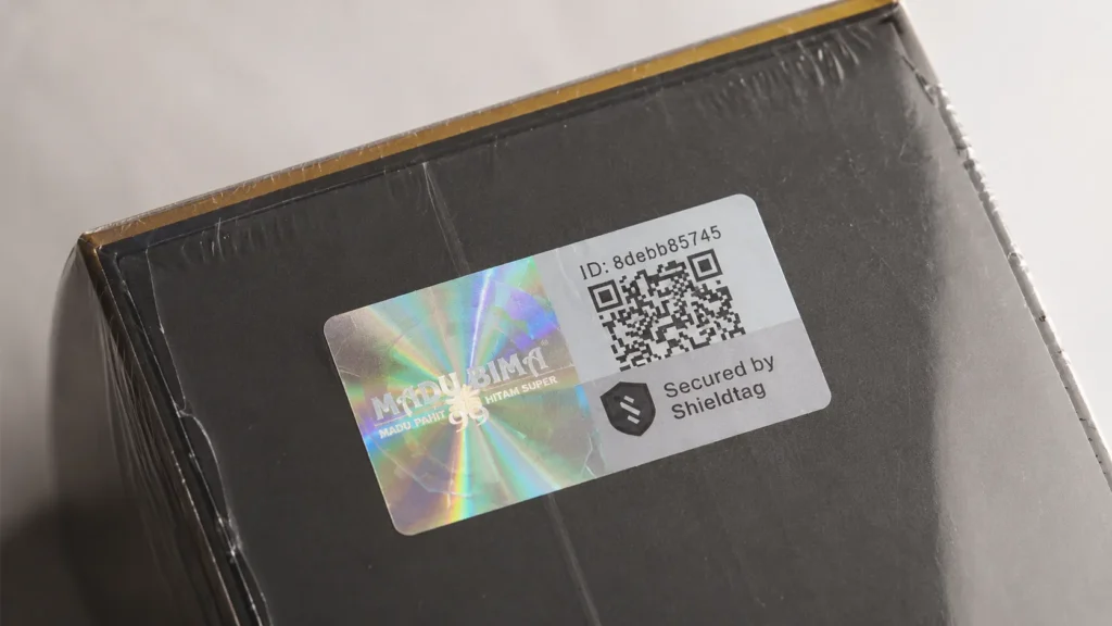 Close-up botol Madu Bima 99 yang menampilkan stiker hologram dan QR-code Shieldtag secara jelas.
